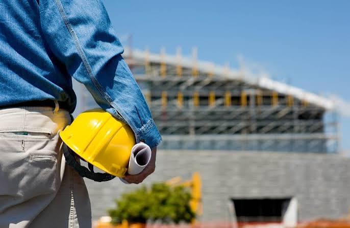 Trabalhador da construção civil com capacete e planta de obra